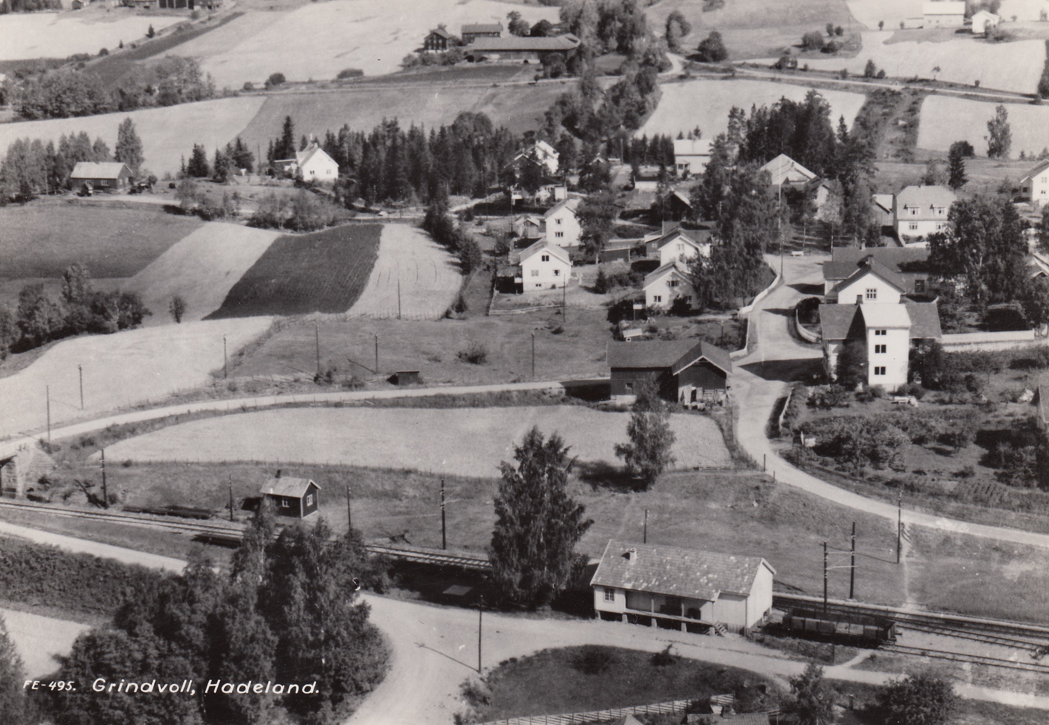 Inntil jernbanesporet ligger Grindvoll innkjøpslag (mjølbua). Flyfotoet fra ca. 1960 er utlånt av Asle I. Jetlund.